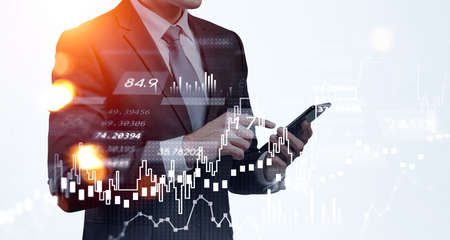 Businessman wearing formal suit is standing and surfing the internet via smartphone. Forex...