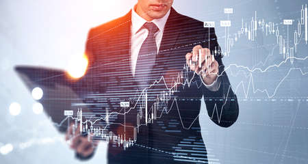 Businessman in formal suit is touching a financial chart with his finger. City skyscrapers in the...