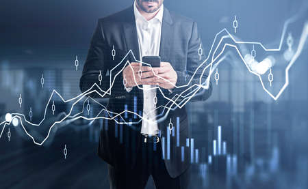 Businessman wearing formal suit is holding smartphone and typing message. Blurred office in the...
