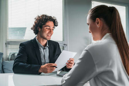 Businessman and businesswoman wearing formal suit are having a conversation about possible promotion. Office workplace in background. Concept of cooperation, teamwork, network and communicationの写真素材