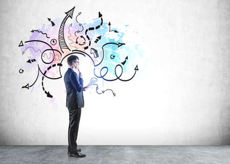 Businessman wearing formal suit is standing in front of the concrete wall with sketch with arrows...