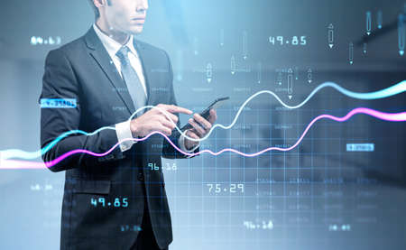 Businessman wearing formal suit is holding and touching screen of smartphone. Blurred office...