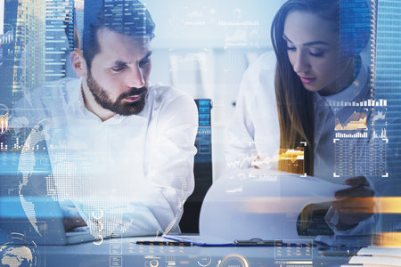 Businessman and businesswoman wearing white shirts work together typing on laptop and taking notes on clipboard. Office workplace and Singapore city skyscraper in the background. Concept of teamworkの写真素材