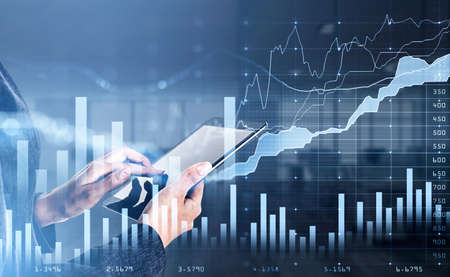 Businesswoman wearing formal suit is holding and touching tablet with her finger. Blurred office...