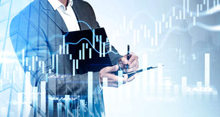 Businessman wearing formal suit is holding and taking notes on clipboard. Financial graph and chart...