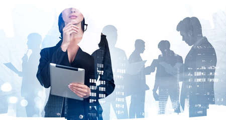 Businesswoman wearing formal suit is holding tablet and touching chin. Silhouettes of group of business people work together for company. Singapore city skyscraper in background. Concept of teamworkの写真素材