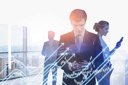 Businessman and businesswoman wearing formal suits are working together holding smartphones. New York city skyscraper panoramic view in background. Digital interface with arrows. Concept of teamworkの写真素材