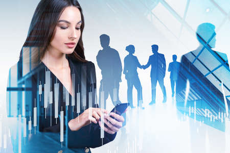 Group of business people wearing formal suits work together using smartphone and shaking hands. City skyscraper in the background. Forex candlestick in foreground. Concept of teamwork and cooperationの写真素材