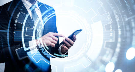 Businessman wearing formal suit is touching smartphone screen with his finger. New York city skyscraper downtown in the background. Digital interface with circle hologram in the foregroundの写真素材
