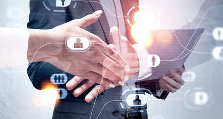 Businessman and businesswoman wearing formal suit shake hands. Man is holding clipboard and reading document. New York city skyscraper in the background. Social media and human resources in foregroundの写真素材