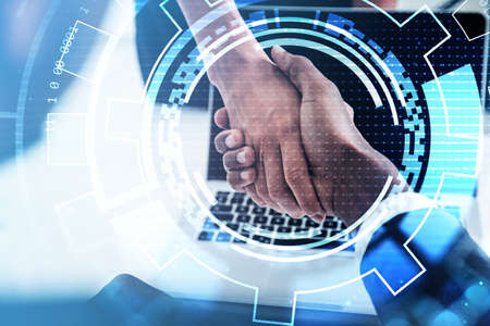 African American businessman shakes hands with businesswoman in formal suit. Office workplace with laptop in the background. Digital interface with circle hologram in the foregroundの写真素材