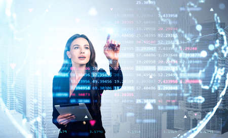 Businesswoman wearing formal suit is touching screen with her hand and holding tablet. Digital interface with virtual globe and chart in foreground. New York city in background. Concept of technologyの写真素材
