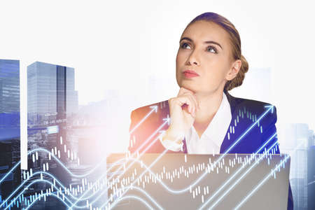 Businesswoman wearing formal suit is holding chin with hand. Digital interface with rising graph and arrows in foreground. New York city in background. Concept of futuristic technologies in businessの写真素材