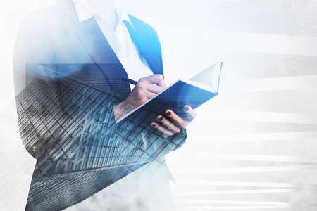 Businesswoman in formal suit taking notes in clipboard. Double exposure with low angle skyscraper faの写真素材