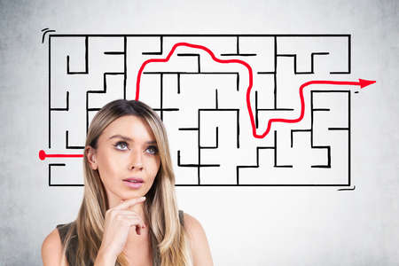Business woman thinking to find a solution, labyrinth on concrete wall on background. Caucasian blonde businesswoman with hand on chin, business solution concept.の写真素材