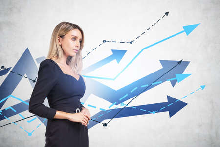 Confident attractive business woman in formal black dress is pondering how to optimize business process to boost sales of the company. Growing line charts with arrows on concrete wallの写真素材