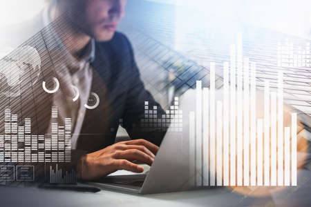 Concentrated young business man or stock trader analyzing stock graph chart using laptop to buy or sell stock, double exposure graph, internet tradingの写真素材