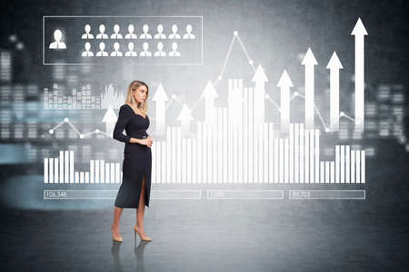 Attractive businesswoman in formal dress standing in empty room, white bar chart with arrows and peoples silhouettes are drawn on dark concrete wall. Human recourses and career opportunities concept.の写真素材
