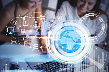 Two smiling businesswoman working on laptop, office interior, blue and white glowing information protection icons and globe. Padlock, business data symbols. Concept of cyber security and data storageの写真素材