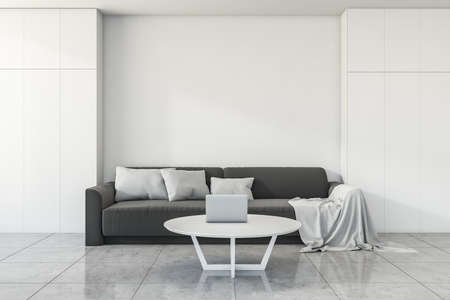 Dark couch in light apartment interior with blanket and pillow, coffee table with laptop on gray concrete floor. Mockup blank wall copy space, 3D renderingの写真素材