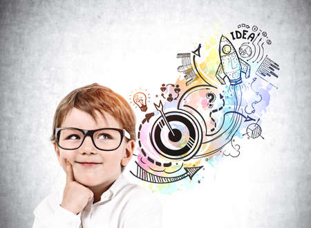 Boy in glasses is standing near sketch with icons of rocket launch, start up, light bulb, globe, bar, pie diagrams, teamwork, plan and arrow. Concept of inspiration and imagination for creative ideaの写真素材