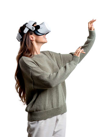 Young attractive businesswoman wearing green sweater and vr helmet is standing and touching air....