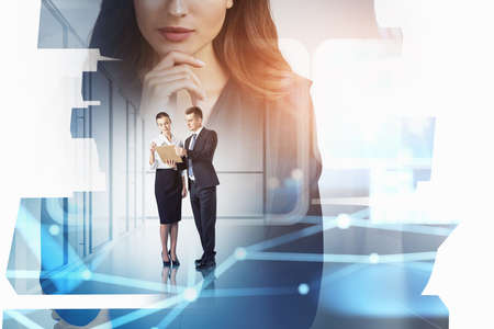 Businessman and businesswoman wearing formal suits work together holding clipboard. Office workplace with panoramic window and city skyscrapers in the background. Concept of teamworkの写真素材