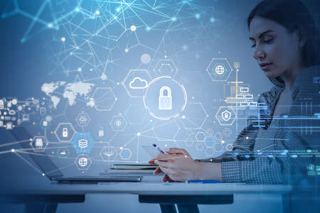 Businesswoman wearing grey dress is typing message on smartphone. Office workplace with digital...