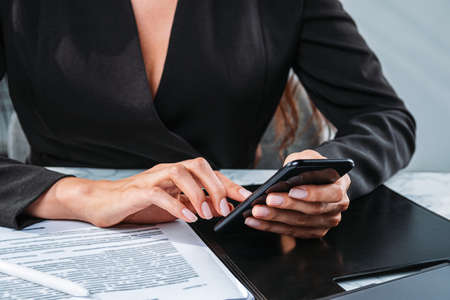 Businesswoman with phone in hands, closeup. Business paper document and clipboard on the table....