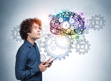 Young man in blue shirt with a pensive look, holding device in hands. Cogwheels and gears on blue...