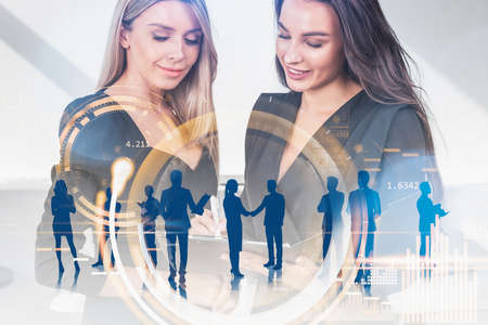 Young attractive businesswomen wearing formal suits work together making deal and sign contract. Digital interface with circle hologram in the background. Concept of teamwork and cooperationの写真素材