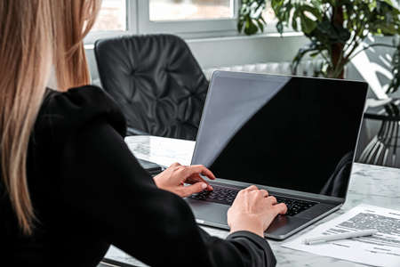 Over the shoulder shot of businesswoman with laptop on the desk, typing on the computer. Manager...