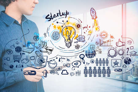 Thoughtful young businessman, casual denim shirt holding his notes in hands, sketch of business icons describes of thinking process to sturt up new business. Panoramic windows with New York city viewの写真素材