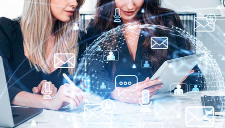 Young attractive businesswoman wearing formal suit is talking to colleague. Office workplace in the background. Digital interface with hologram of virtual globe in the foreground. Concept of teamworkの写真素材