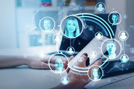 Office woman using smartphone and laptop in office room. Blue hud glowing hologram with diverse people portraits, double exposure. Concept of technology and human resourcesの写真素材