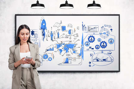 Businesswoman wearing formal coat is standing and holding smartphone in front of sketch with rocket...