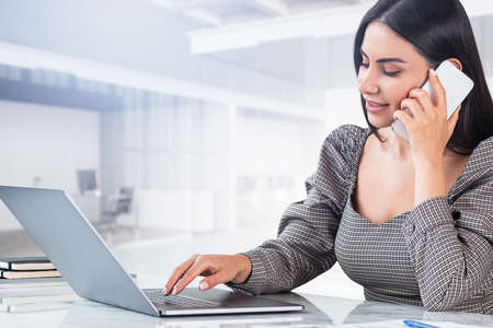Secretary woman talking on the phone, typing on laptop keyboard. Background of business room with...