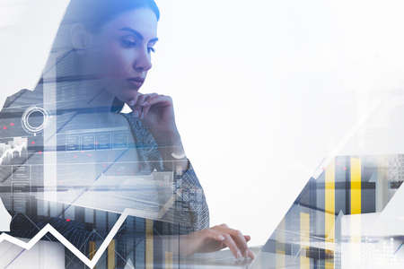 Businesswoman is typing message on laptop. Financial chart and graph with rising arrow in the foreground. City skyscraper downtown center in background. Concept of trading and digital interfaceの写真素材