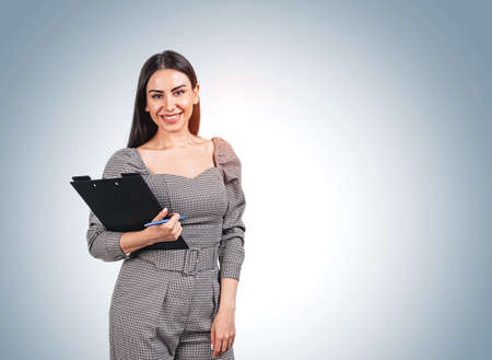 Woman standing in jumpsuit, happy look, business documents in hands, blue background. Mockup copy space blank wall. Concept of businesswoman and plansの写真素材