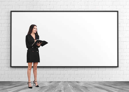 Woman standing in black formal wear, take note, business documents in hands, brick wall and parquet floor. Mockup copy space canvas. Concept of startup and projectの写真素材