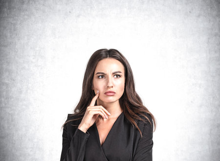 Office woman in black dress with confused, serious look on gray background. Boss making up plans and new ideas. Concept of brainstorm. Copy space blank wallの写真素材