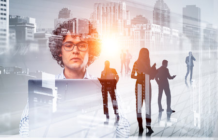 Young man in eyeglasses using computer, silhouettes of business people talking and working together, double exposure of New York buildings. Concept of distance learningの写真素材