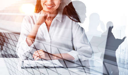 Office woman in white shirt, smiling, business papers on desk. Double exposure of business buildings and people teamwork. Concept of contract and international companyの写真素材