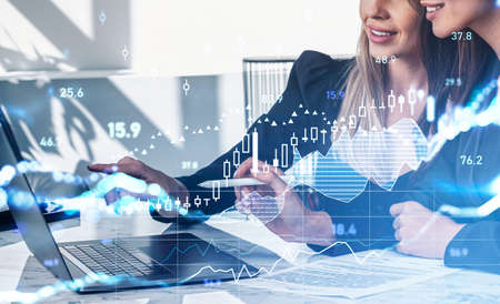 Two businesswomen wearing formal suits work together analyzing stock market on laptop. Office...