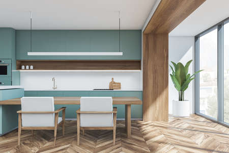 Minimalist green and white kitchen interior with linear light over breakfast bar table, panoramic...