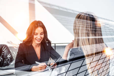 Two office women have a conversation, smiling. Recruitment interview in financial company, human resources. Concept of career development and jobの写真素材