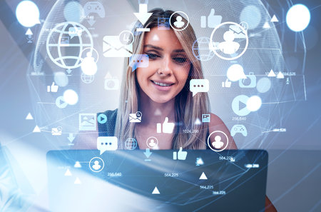 Businesswoman wearing formal dress is looking into laptop. Office workplace in the background. Social media Icons of virtual globe, message, play, camera. Concept of internet communicationの写真素材