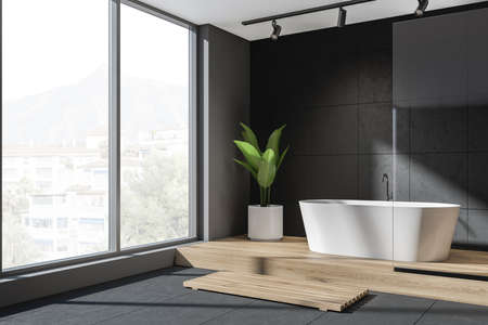 Black bathroom interior, tub on wooden podium with plant in the corner, side view. Modern bathing room with tiled floor and panoramic window on countryside, 3D renderingの写真素材