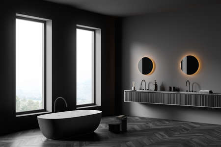 Gray bathing room interior with tub and table with towel, two sinks, round mirrors with backlight and accessories on black wooden deck, parquet floor and window on countryside, 3D renderingの写真素材