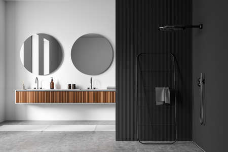 Stylish bathroom interior with black corner with douche, two sinks with round mirrors on white wall, towel rail ladder on gray concrete floor, 3D renderingの写真素材